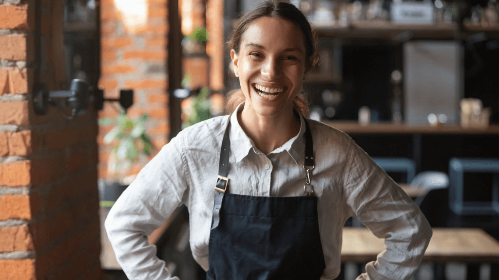 Cheerful young waitress wearing apron laughing looking at camera