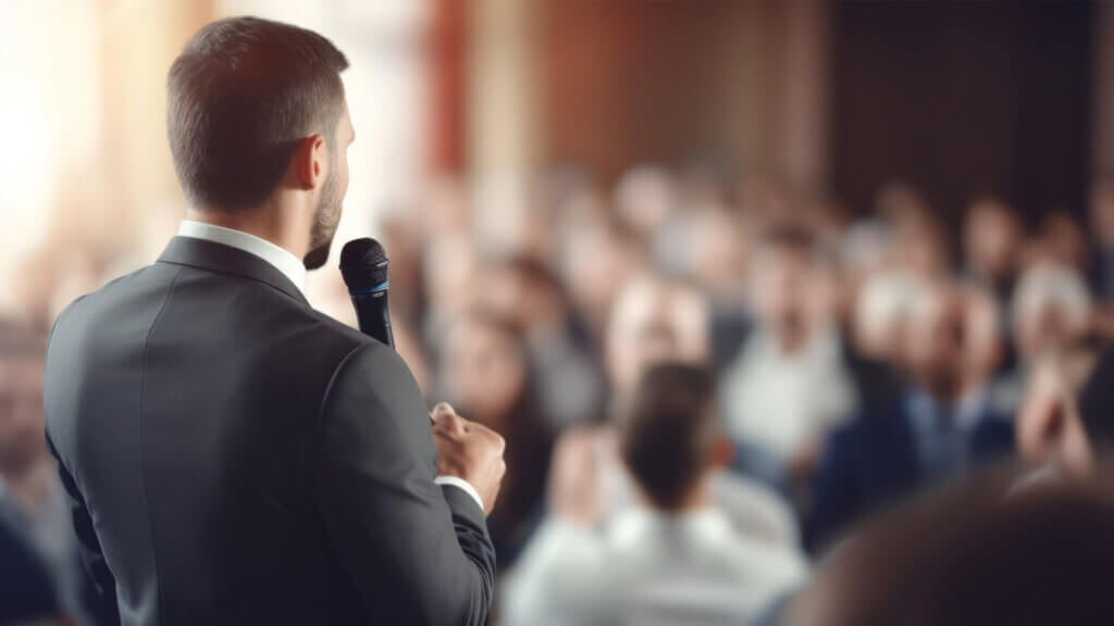 Back view of Man in business suit giving a speech on the stage in front of the audience